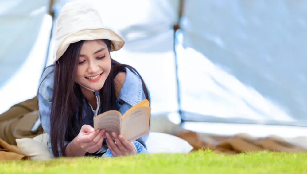 Digital Detox Retreat | Person laying on floor reading book under a tent canopy.